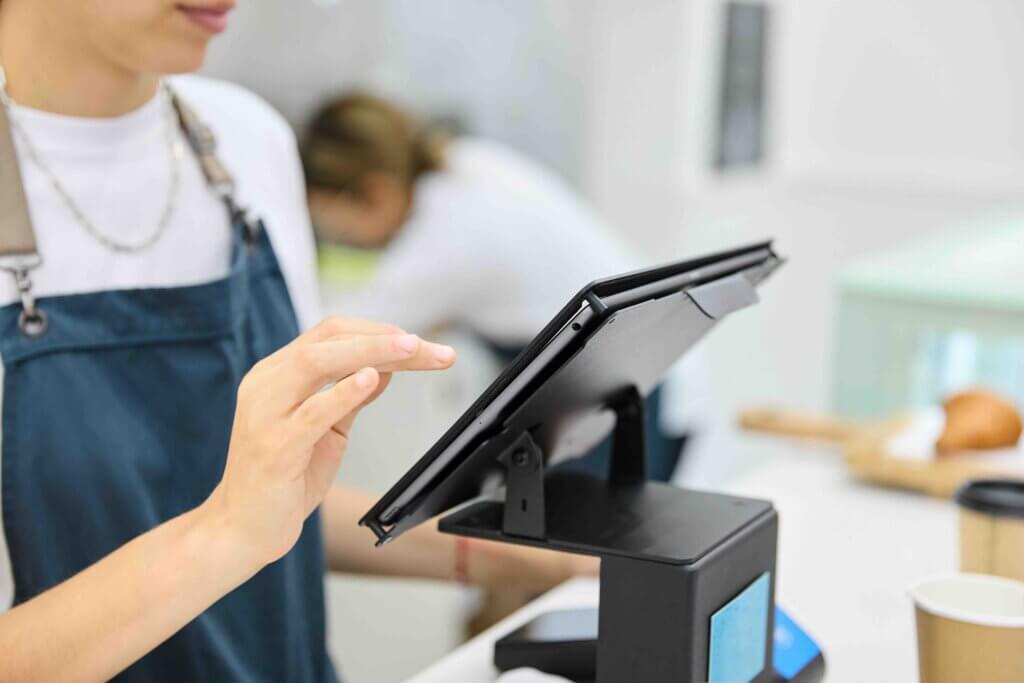 Barista at cafe counter entering customer order on digital tablet.