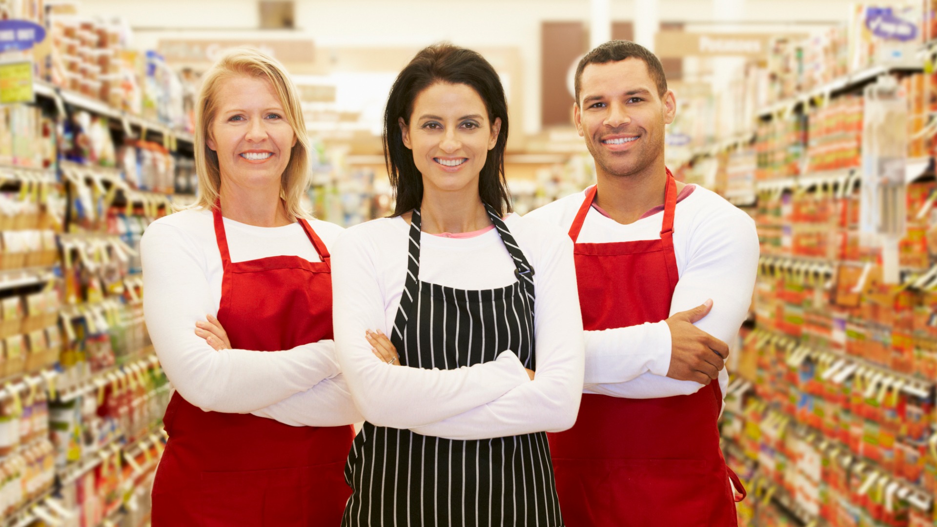 three employees wearing aprons in grocery store aisle