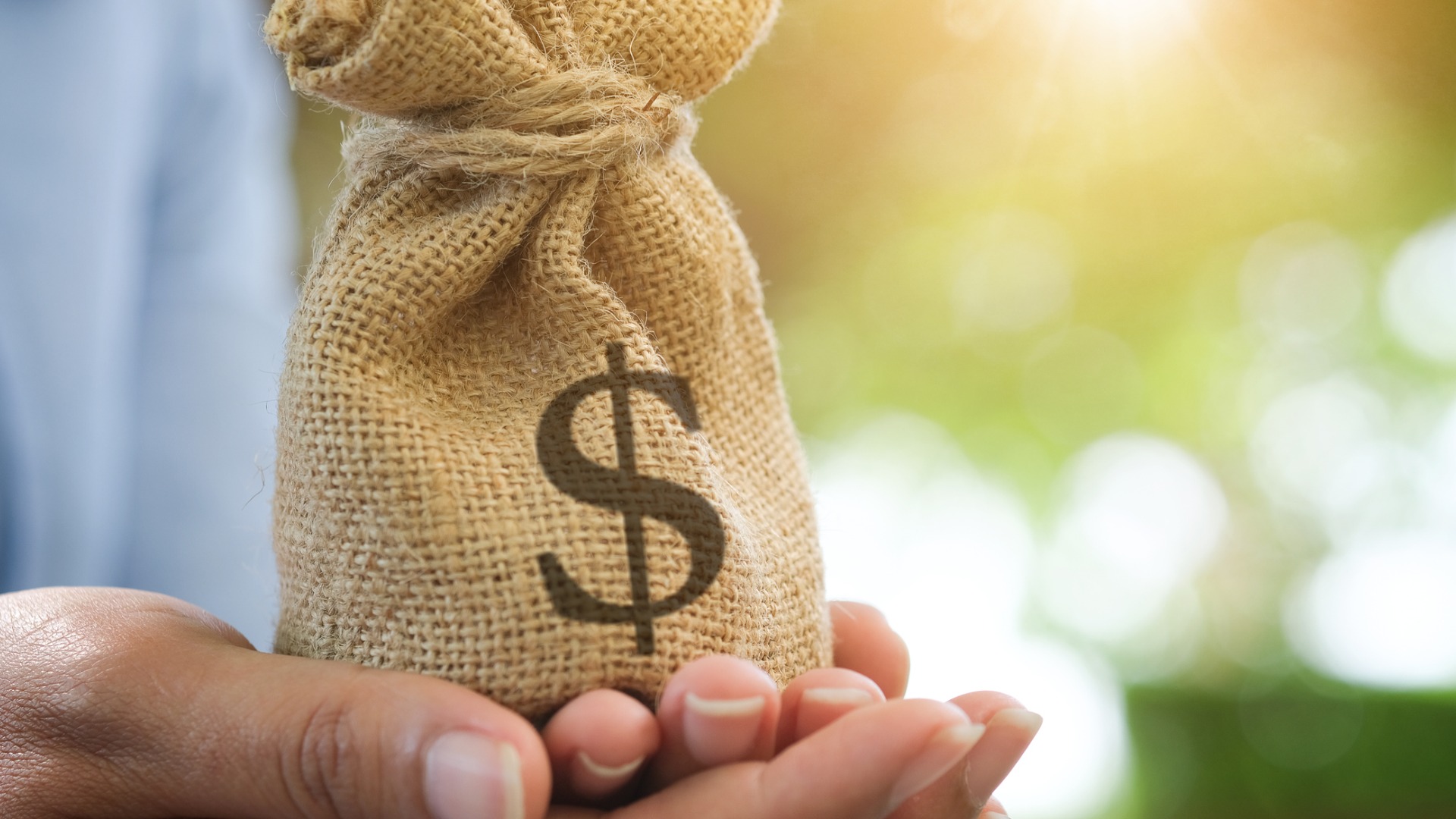 hands holding small burlap sack with $ on it