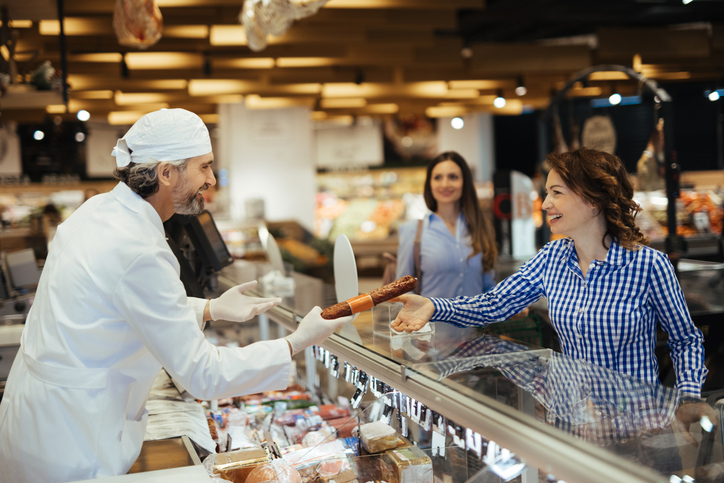 Female customer buying sausage from deli counter in supermarket