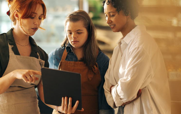Supermarket manager using a digital tablet while having a discussion with her employees in a staff meeting. Group of diverse women working together in an all-female small business.