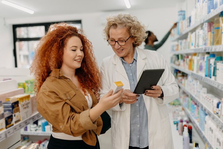 Using modern technology in the pharmacy. Female pharmacist and customer looking at tablet
